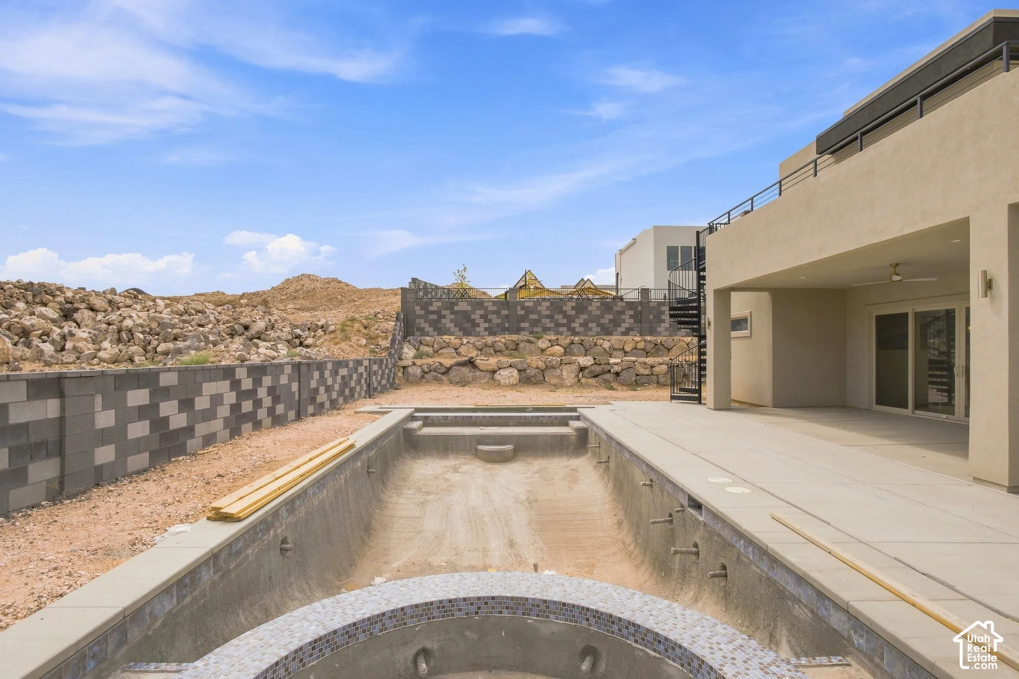 Pool under construction with integrated spa, adjacent to a ground-level patio and a spiral staircase providing upper-level access