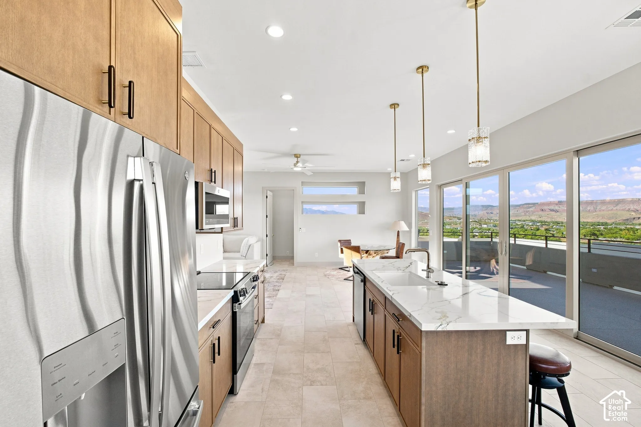 Gourmet kitchen with stainless steel appliances, wood-finish cabinetry, a large center island with a sink, and sliding glass doors to the exterior