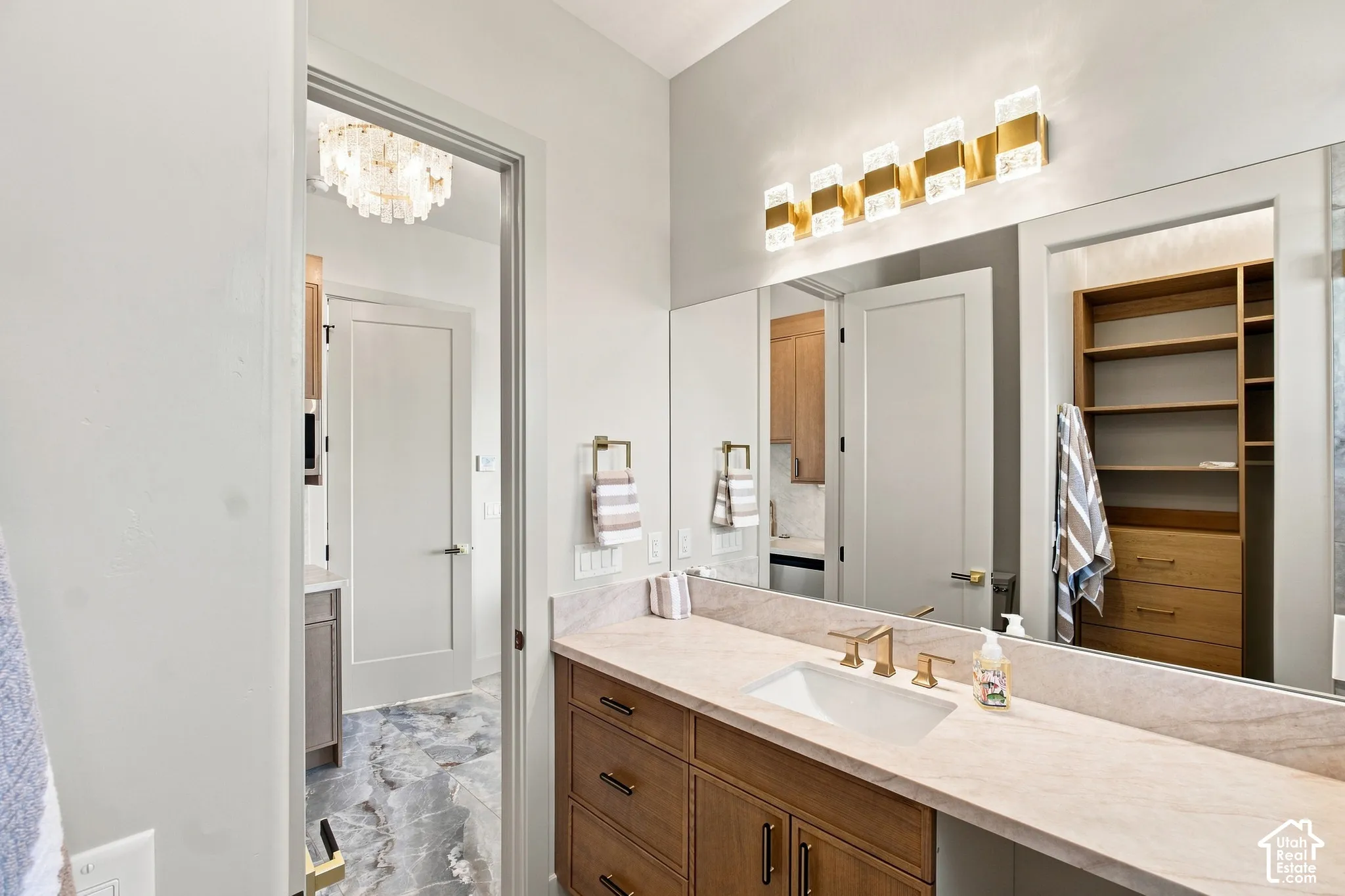 Vanity with a single undermount sink, brass finish faucet, light-toned countertop, and wood-finish cabinetry
