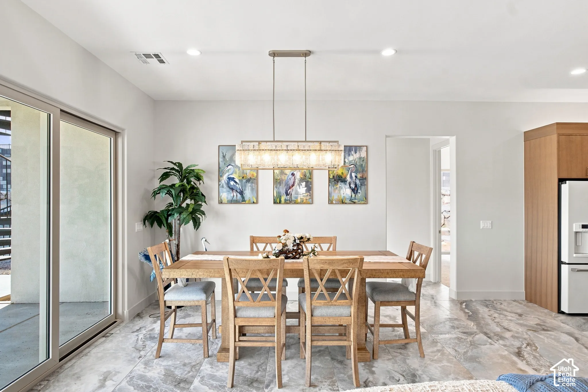 Recessed ceiling lighting, linear chandelier, sliding glass door, wood cabinetry, and large format floor tiling