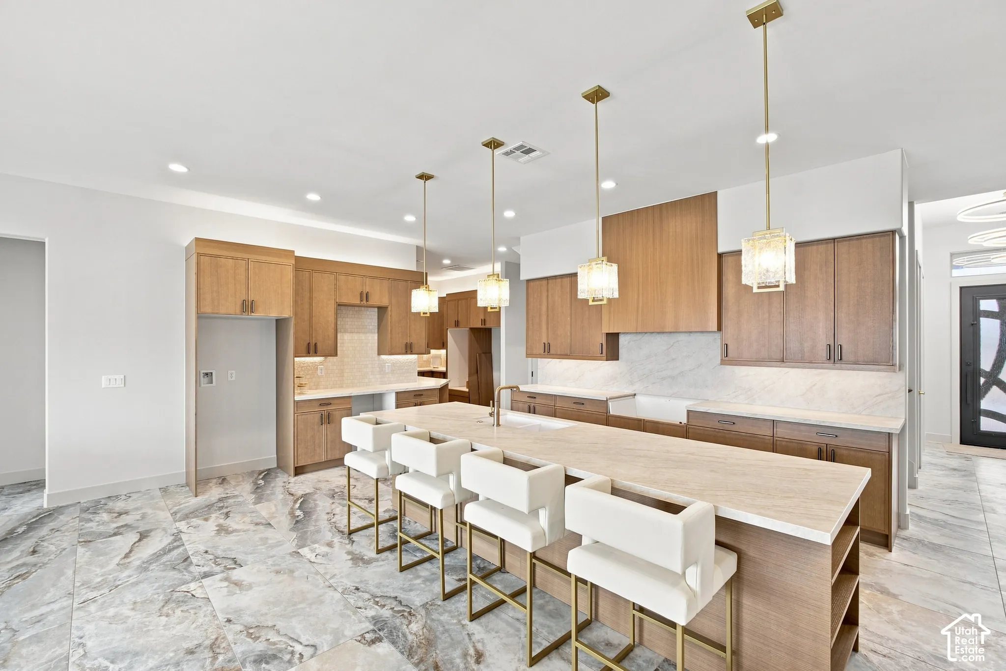 Spacious kitchen featuring an expansive island, light wood-finish cabinetry, patterned stone flooring, undermount sink, and recessed lighting