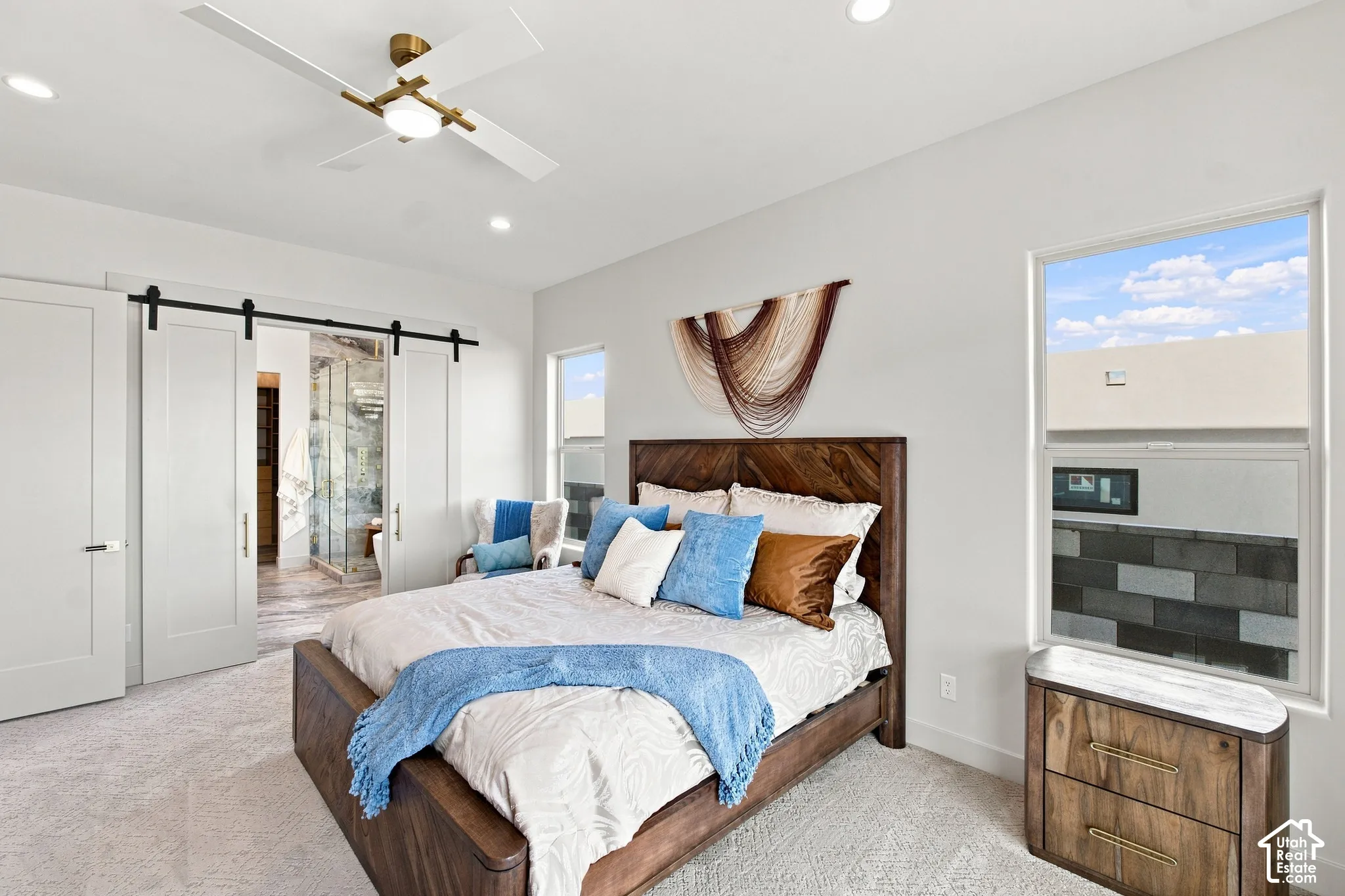 Recessed lighting, ceiling fan with light, barn doors, wood-finish bed frame, and wood-finish nightstand with a light-toned top