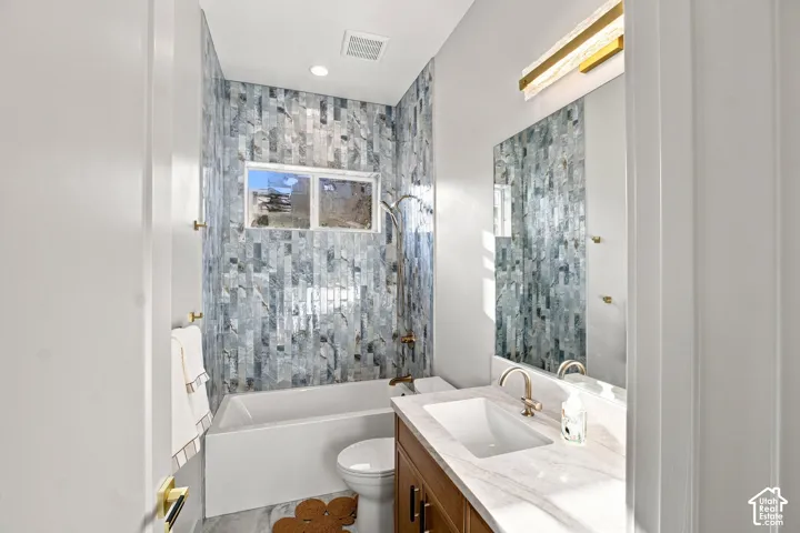 Porcelain bathtub with an iridescent tile surround, a single window, and a vanity featuring a rectangular undermount sink