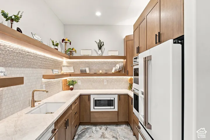 Wood-finish cabinetry, under-cabinet lighting, integrated microwave, built-in double ovens, and a white integrated refrigerator