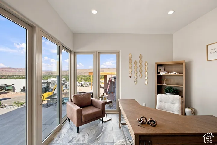 Expansive glass sliding doors, additional window panels, recessed ceiling lighting, L-shaped wood-finish desk, and built-in shelving