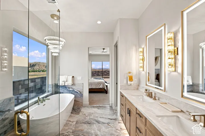 Freestanding soaking tub with a window, dual vanity with undermount sinks, illuminated mirrors, and a glass-enclosed shower