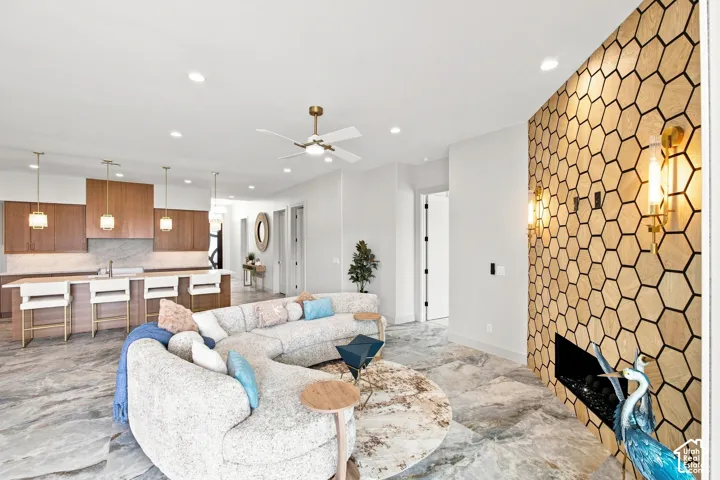 Open-concept living area featuring a fireplace with a hexagonal wood accent wall and integrated lighting, a ceiling fan, recessed lighting, and large-format tile flooring