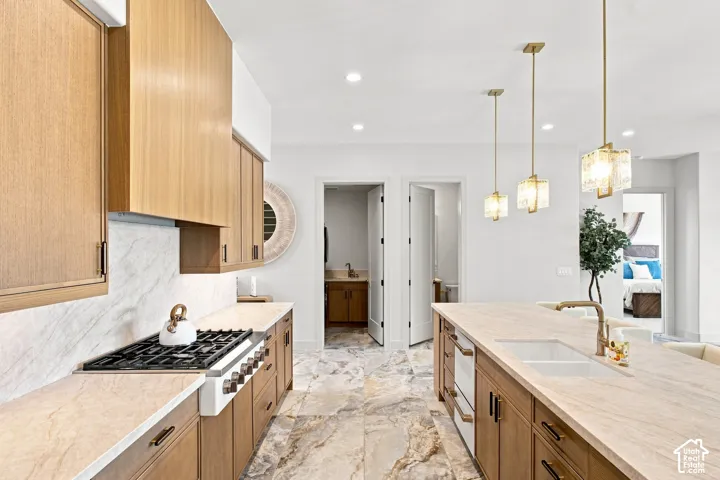 Gourmet kitchen with light wood-finish cabinetry, stone flooring, integrated range, and a large center island with a built-in sink