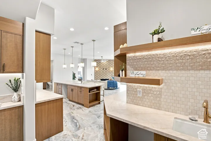 Wood-finish cabinetry, light-colored countertops, large format floor tiles, illuminated open shelving, and a mosaic tile backsplash