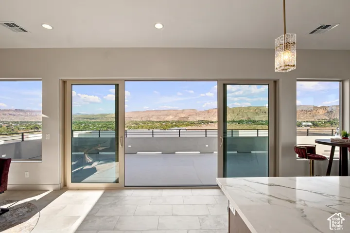 Sliding glass door opening to a concrete patio with black railings, recessed lighting, and a linear pendant light