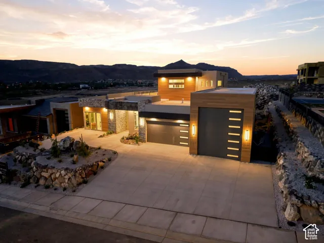 Modern architectural design featuring stacked stone accents, wood-finish exterior panels, an integrated two-car garage, and a concrete driveway