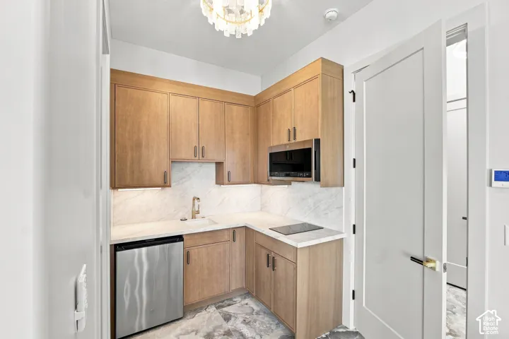 Compact kitchen featuring wood-finish cabinetry, under-cabinet lighting, stainless steel appliances, and a built-in cooktop