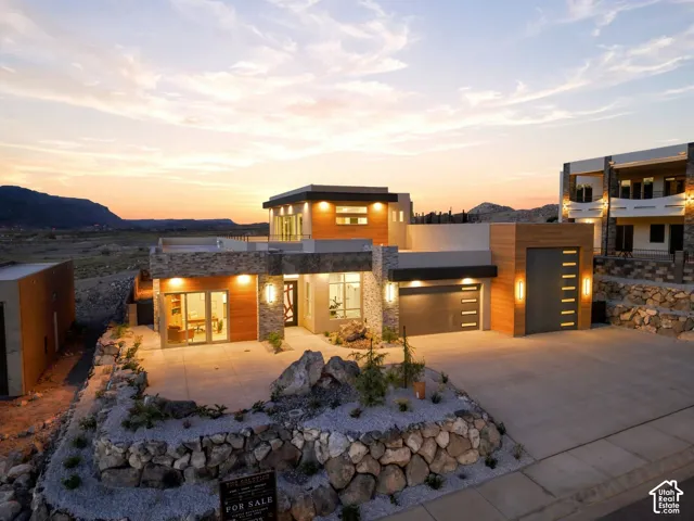 Modern architectural design featuring stacked stone accents, wood-finish paneling, multiple garage bays, and a concrete driveway