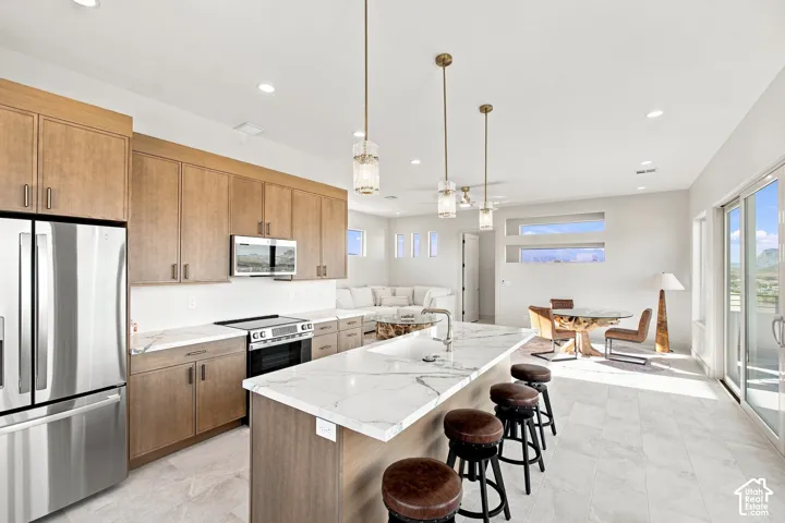 Kitchen island with a waterfall edge, stainless steel appliances, wood-finish cabinetry, recessed lighting, and sliding glass doors