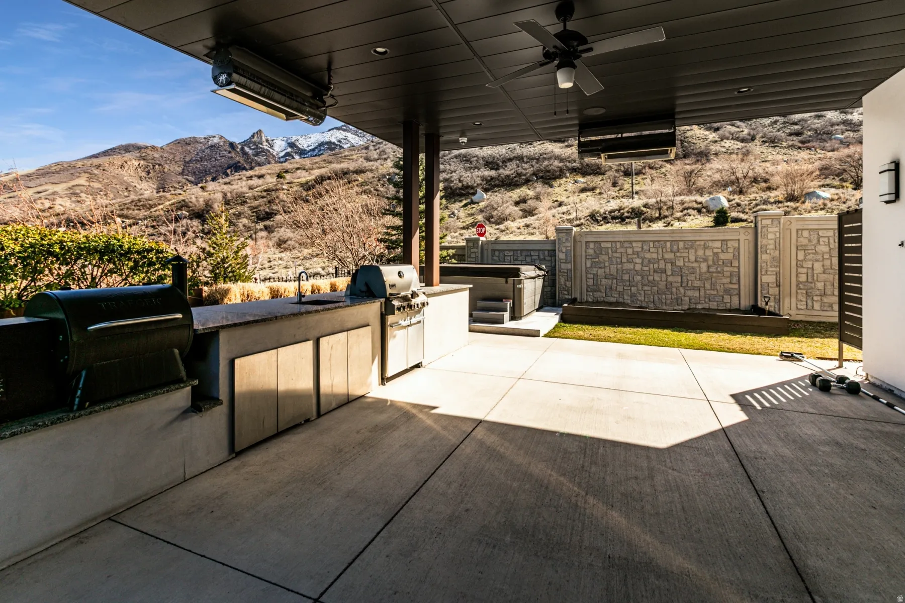 Expansive outdoor patio featuring a built-in outdoor kitchen with integrated sink, a hot tub, and concrete hardscaping