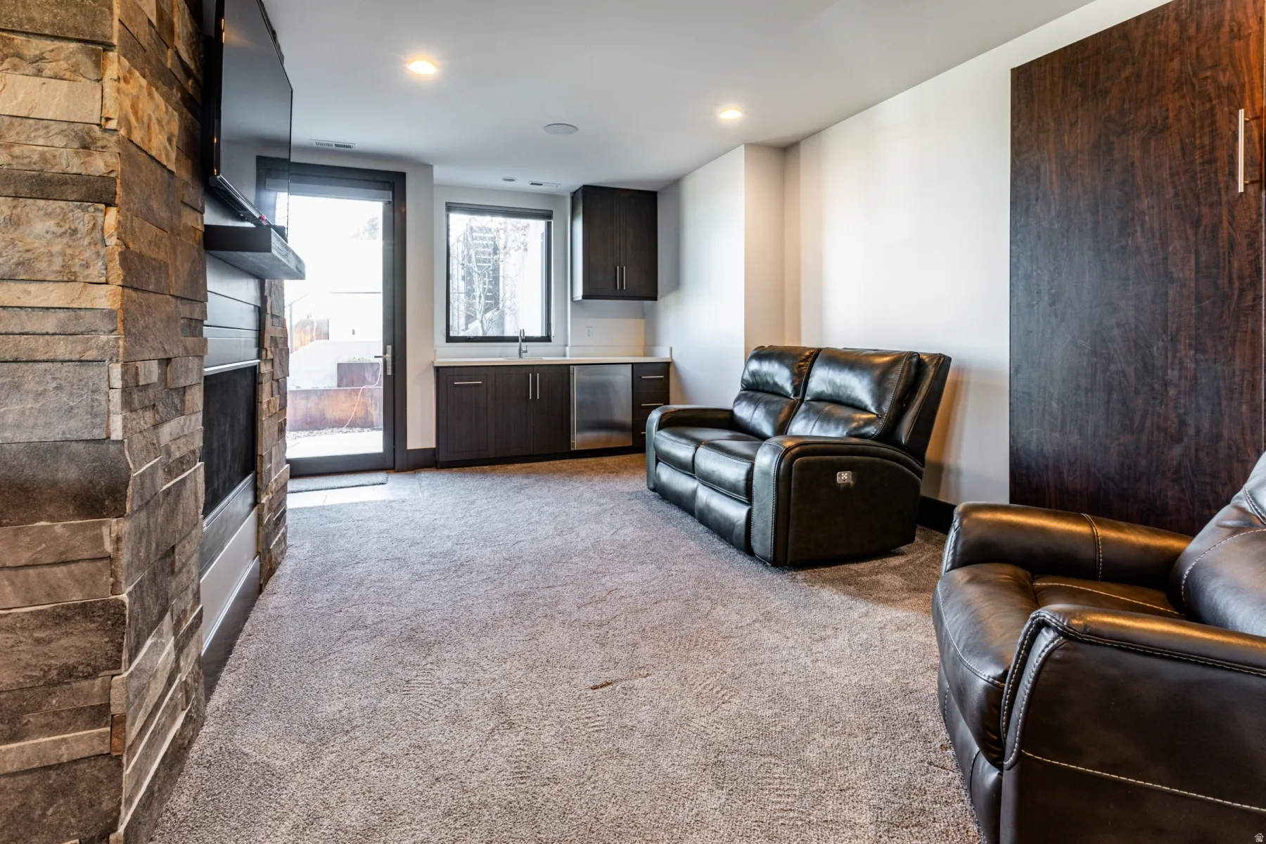 Entertainment space featuring a stone-clad fireplace, integrated shelving, and recessed lighting and wall bed