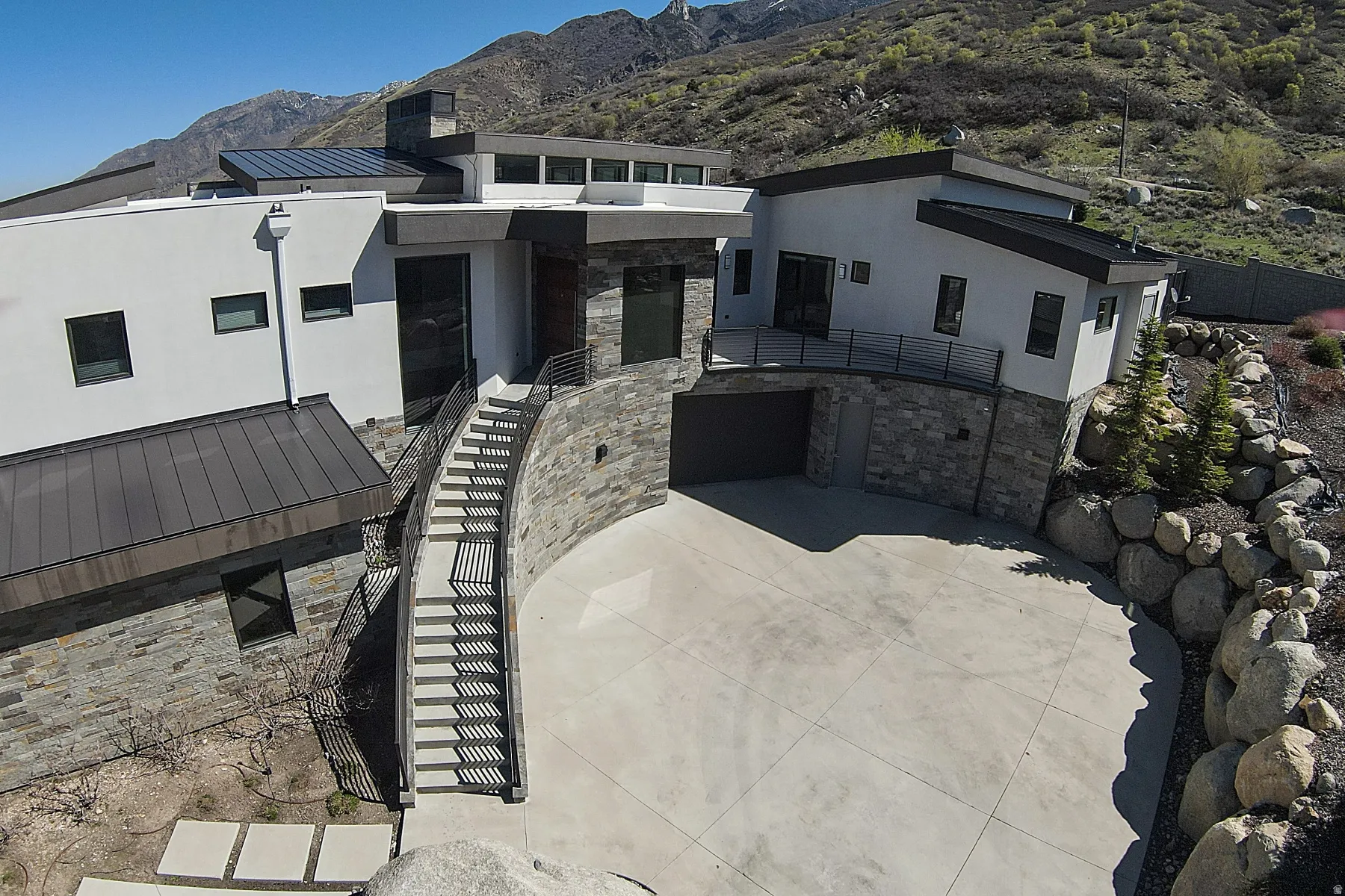 Contemporary architecture featuring a multi-level design with stone accents, stucco siding, a multi-car driveway, and integrated garage