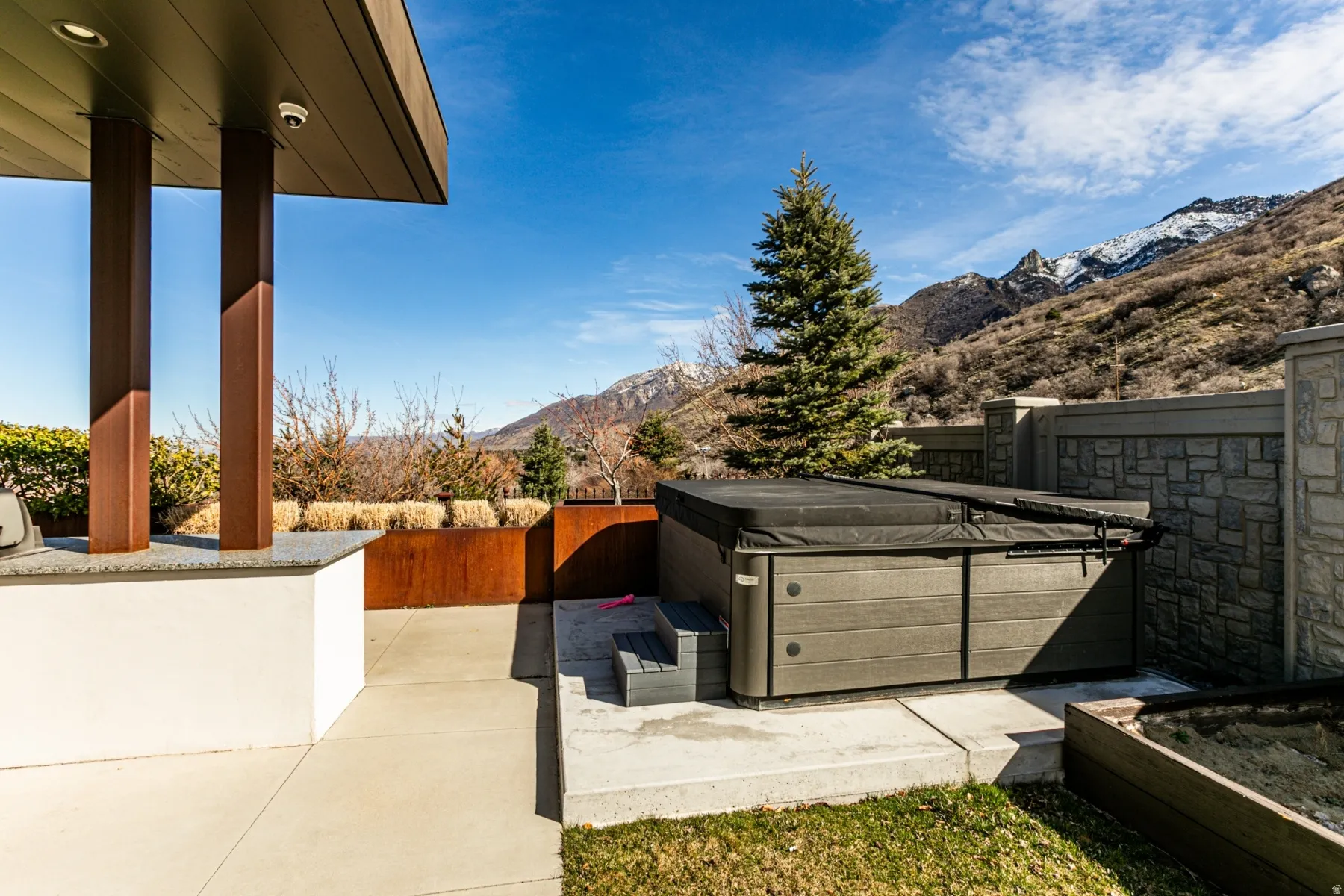 Outdoor patio featuring a hot tub with cover, built-in counter with a light-colored countertop, and a stone wall
