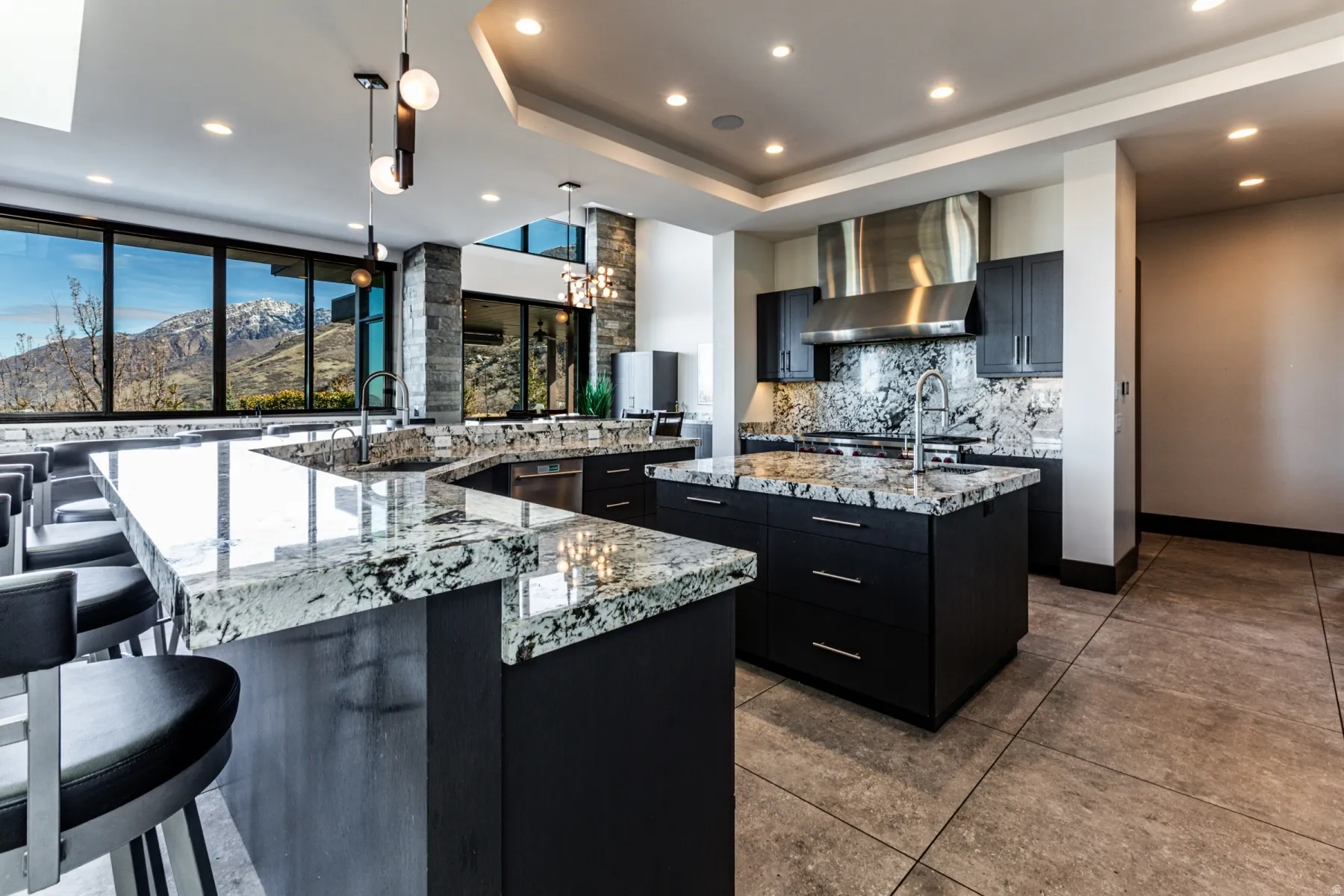 Modern kitchen featuring expansive counter space, a central island, dark cabinetry, stainless steel appliances, and large windows with mountain scenery