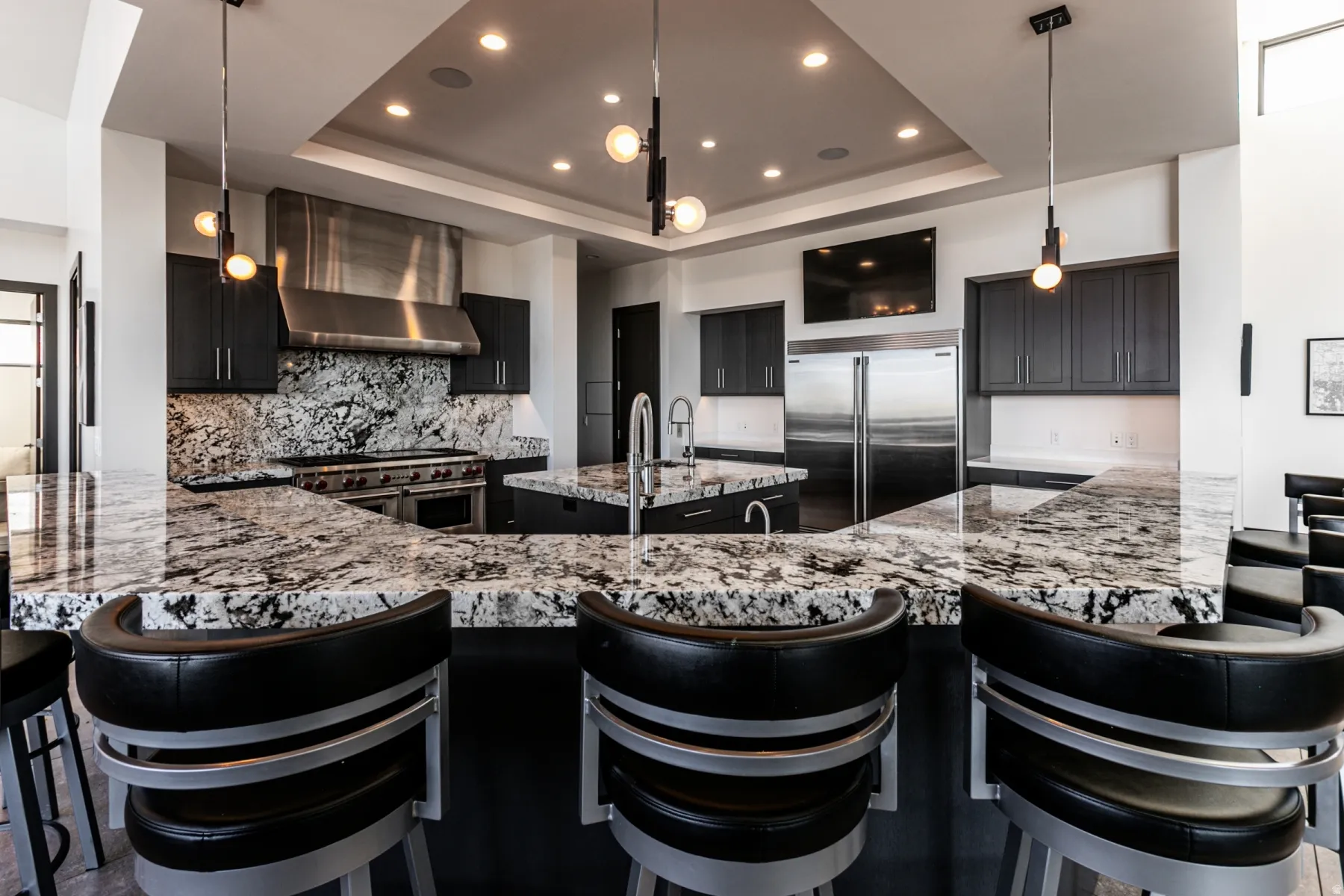 Gourmet kitchen featuring a large island with seating, a professional-grade range with a stainless steel hood, custom dark cabinetry, and integrated stainless steel appliances