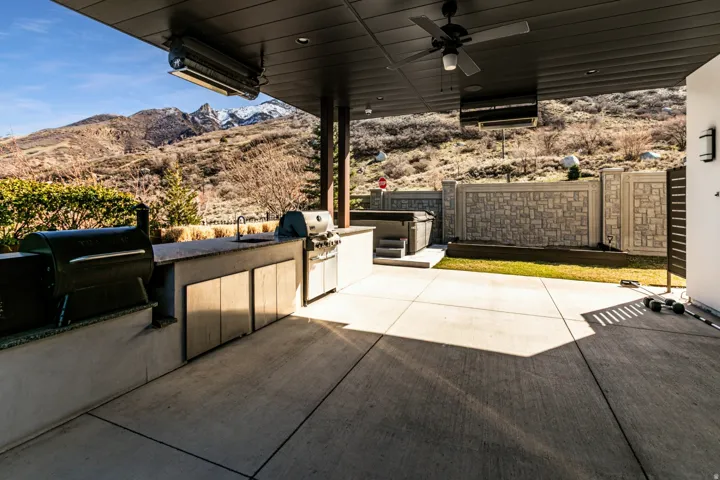 Expansive outdoor patio featuring a built-in outdoor kitchen with integrated sink, a hot tub, and concrete hardscaping