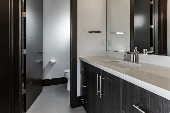 Bathroom 3 featuring a dark wood-finish vanity with an integrated rectangular sink and light-toned countertop, brushed nickel fixtures, a large wall-mounted mirror, and tile flooring