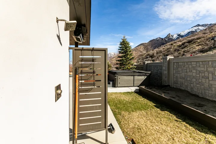 Outdoor shower with modern privacy screen, accompanied by a hot tub, stone retaining wall, and raised planter bed