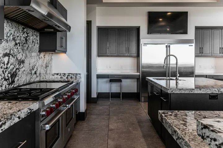 Gourmet kitchen featuring a professional-grade range, stainless steel appliances, granite countertops, dark cabinetry, and a large center island with an integrated sink
