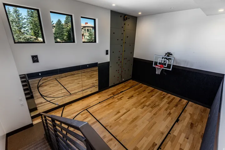 Dedicated indoor activity space featuring wood-finish flooring with court markings, a mounted basketball hoop, and a rock climbing wall