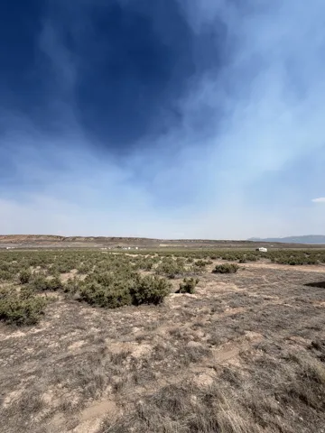 Expansive undeveloped land featuring natural desert vegetation, distant rolling hills, and a vast open sky