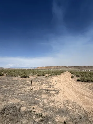 Expansive open terrain with a dirt path, distant natural rock formations, and sparse vegetation under a clear sky