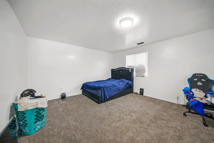 Spacious room featuring neutral carpeting, white walls, a single window with blinds, and a flush-mount ceiling light fixture