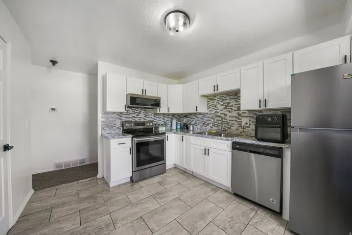 Contemporary kitchen featuring white cabinetry, stainless steel appliances, a mosaic tile backsplash, and light-toned tile flooring