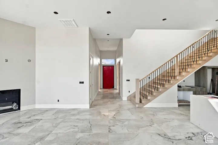 Spacious interior featuring large format tile flooring, a prominent wooden staircase with metal balusters, a built-in fireplace, recessed lighting, and a brightly colored entry door
