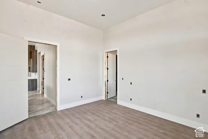 Wood-finish flooring with white baseboards, recessed ceiling lighting, and a white interior door