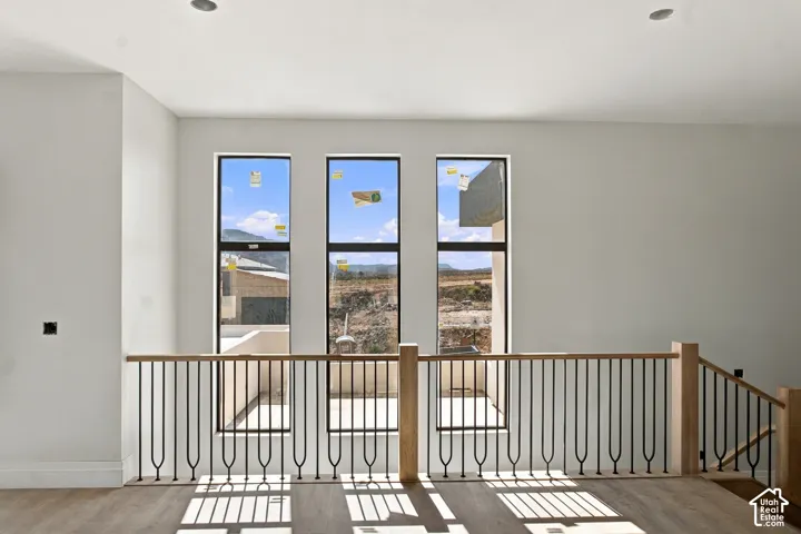 Three large vertical windows, wood-finish flooring, recessed ceiling lighting, and a contemporary black iron and natural wood railing