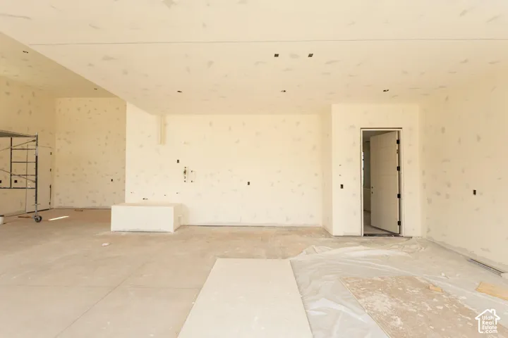 Spacious interior room with an unfinished concrete floor, recessed ceiling lighting, and a modern paneled door