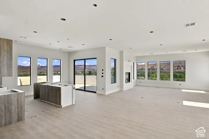 Expansive open-concept room featuring light wood-finish flooring, recessed lighting, multiple large windows, a sliding glass door, and a built-in fireplace