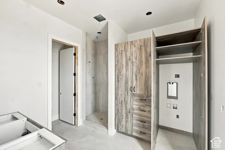 Walk-in shower with tiled surround and floor, wood-finish cabinetry, and built-in shelving