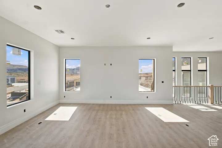 Recessed lighting, wood-finish flooring, multiple windows, white walls, and a black metal and wood railing