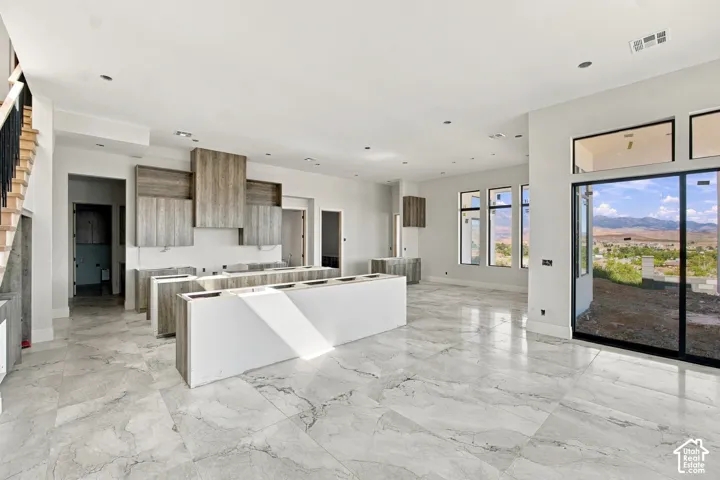 Spacious open-concept interior featuring large format tile flooring, modern cabinetry, dual kitchen islands, and expansive windows with black frames