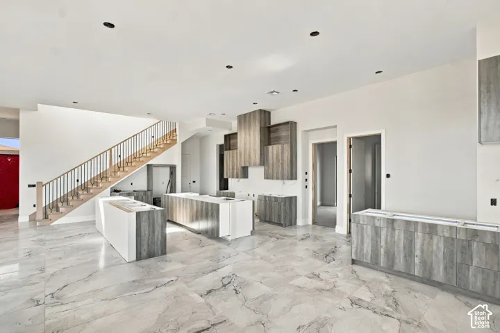 Expansive marble-finish flooring throughout, custom wood-finish cabinetry, two kitchen islands with white bases, and a wooden staircase with metal balusters
