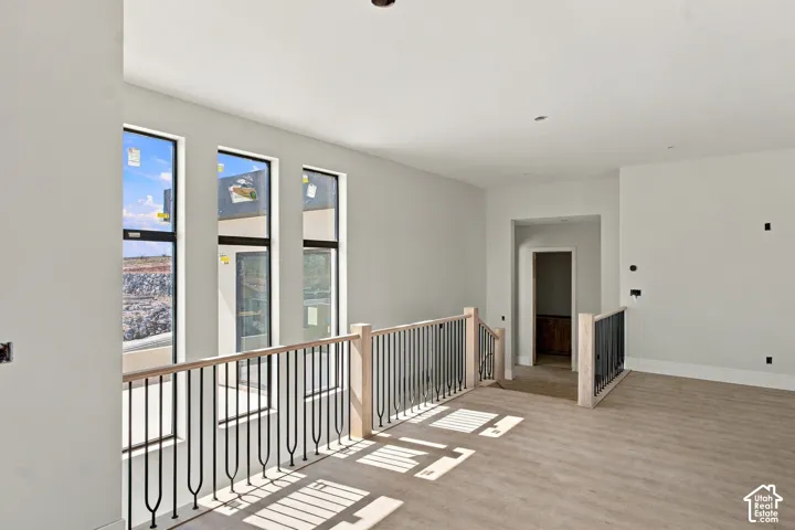 Wood-finish flooring, white walls, black framed windows, light wood newel posts, and black metal balusters