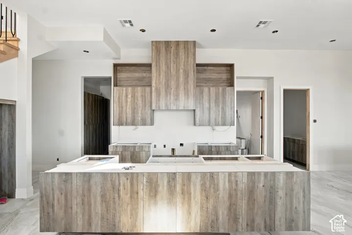 Central kitchen island with wood-finish cabinetry, coordinated wall-mounted cabinetry, and recessed lighting