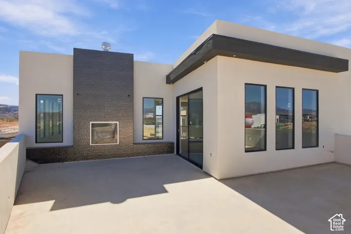 Expansive concrete patio with an outdoor fireplace featuring a textured dark tile surround and two vertical windows