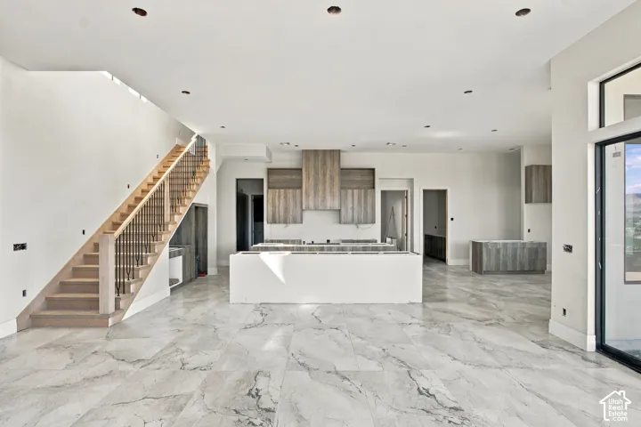 Open-concept living space featuring wood-finish cabinetry, a large kitchen island, and a prominent staircase with iron balusters