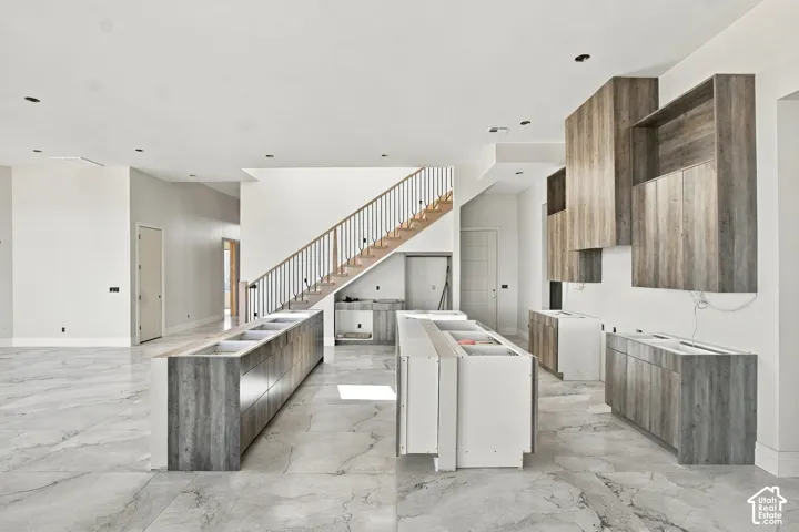 Spacious open-concept interior featuring large format tile flooring, a multi-level staircase with wood handrails, and recessed ceiling lighting
