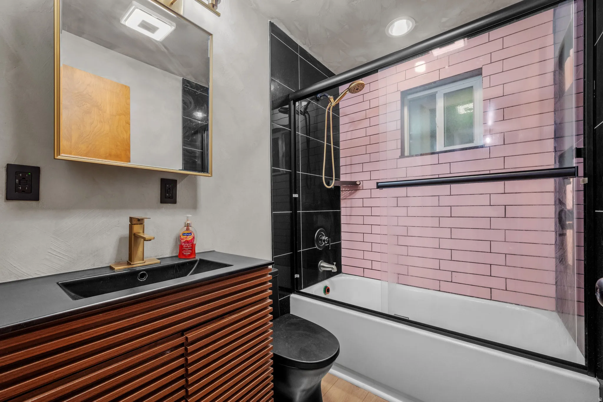 Bathroom featuring a vanity with a dark countertop and wood-finish cabinetry, a black toilet, and a bathtub with a clear glass sliding door