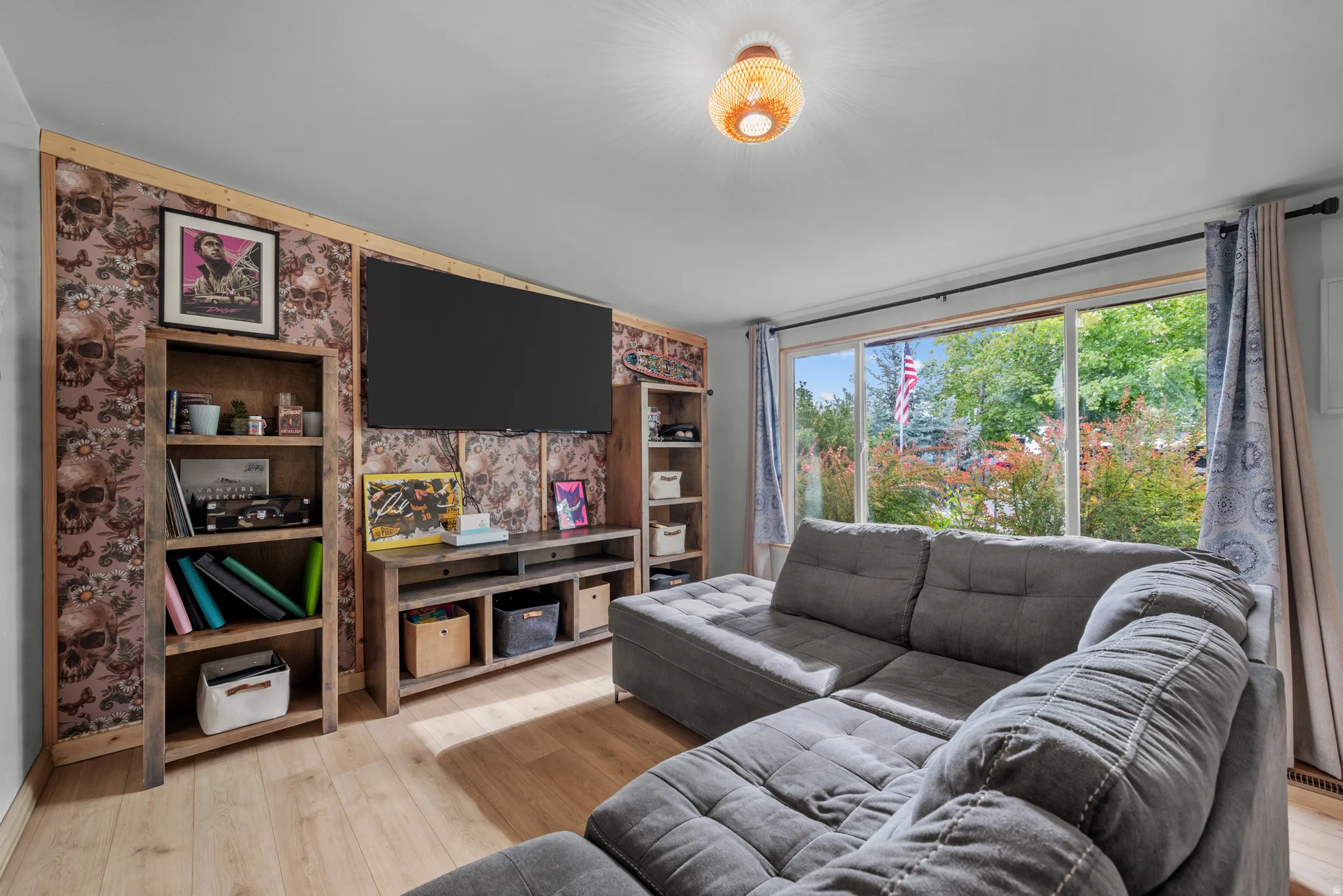 Spacious living area featuring wood-finish flooring, a decorative accent wall, and a ceiling-mounted light fixture