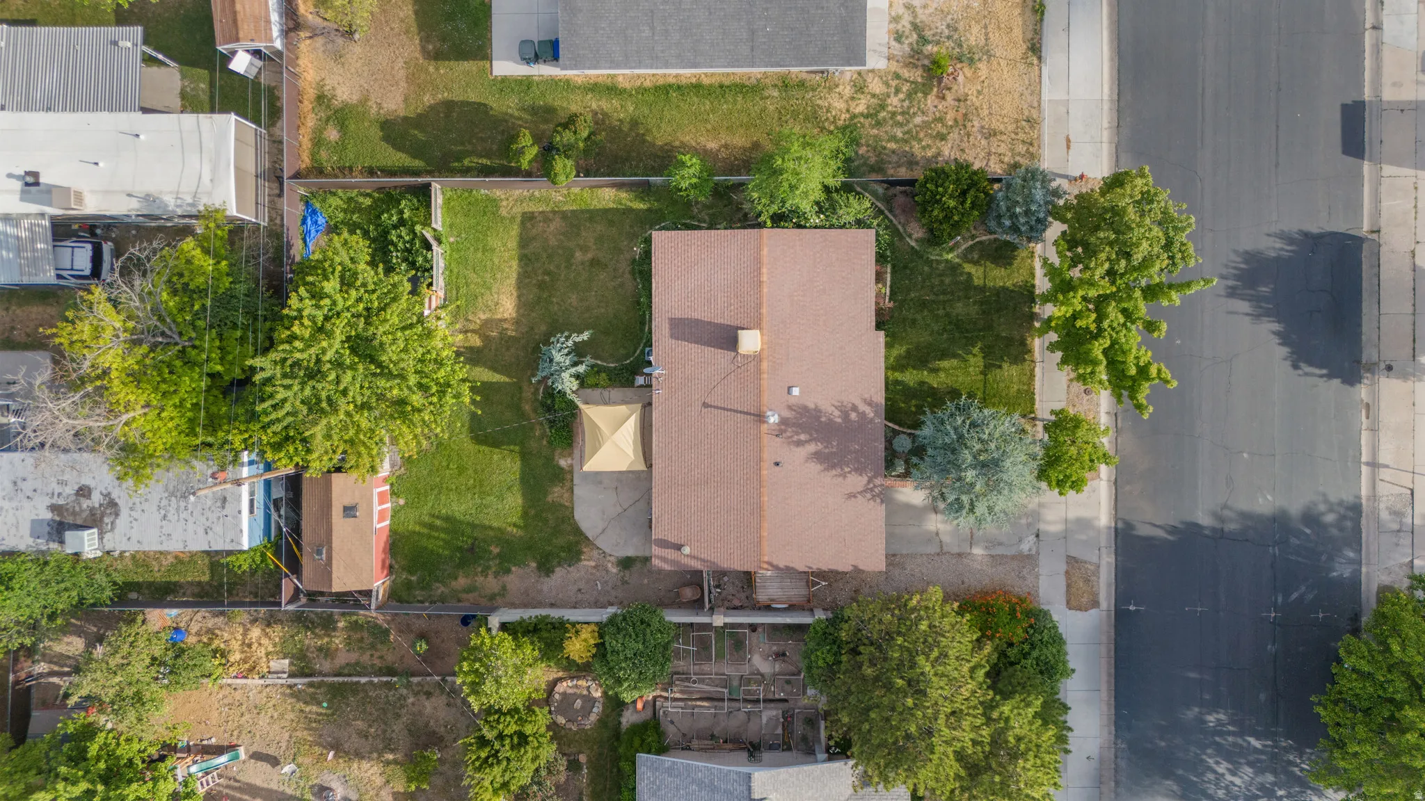 Aerial perspective showcasing a property with a brown shingle roof, a large grassy yard, and mature landscaping